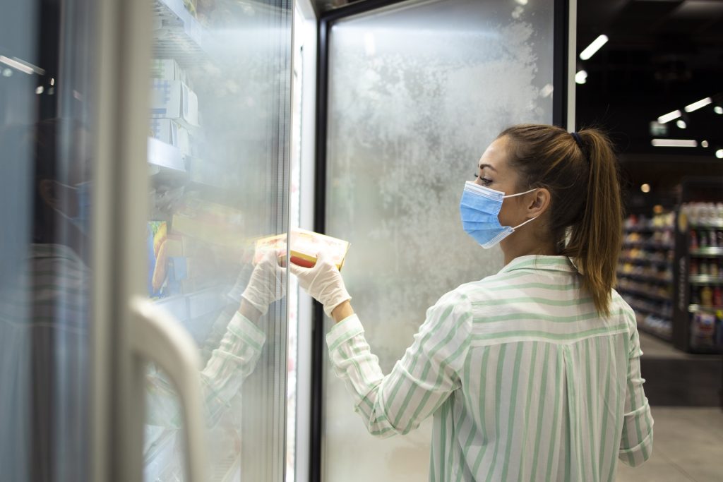 Woman buying food in supermarket and protecting herself against highly contagious corona virus pandemic.