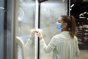 Woman buying food in supermarket and protecting herself against highly contagious corona virus pandemic.